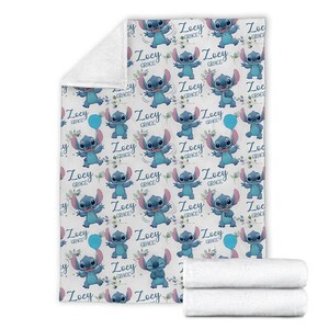 May include: A white fleece blanket featuring a repeating pattern of the blue character Stitch from Lilo and Stitch, interspersed with green leafy sprigs, blue balloons, and the name Zoey Grace written in a dark blue script font throughout the design.