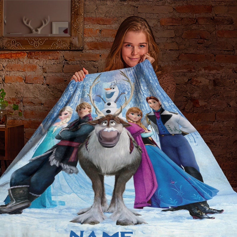 May include: A soft fleece blanket featuring a printed graphic of characters from the movie Frozen, including Elsa, Anna, Kristoff, Olaf, and Sven the reindeer. The design is set against a snowy, icy blue background with the word NAME at the bottom.