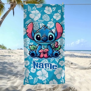 May include: A blue beach towel featuring a cartoon character holding a pink flower. The towel has a white floral pattern on a blue background. The word "Name" is printed in blue on the bottom.