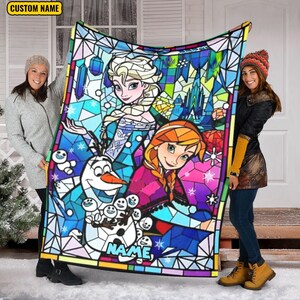 Pode incluir: Uma manta retangular com uma estampa estilo vitral de dois personagens animados com cabelos tran&ccedil;ados e um boneco de neve. O design inclui formas geom&eacute;tricas em azul, rosa e amarelo, com o texto CUSTOM NAME na parte superior.