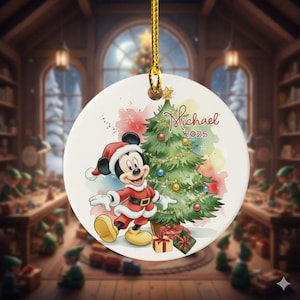 May include: A round Christmas ornament featuring Mickey Mouse in a Santa suit next to a decorated Christmas tree. The ornament has the name "Michael" and the year "2025" on it. The ornament is white with a gold string.