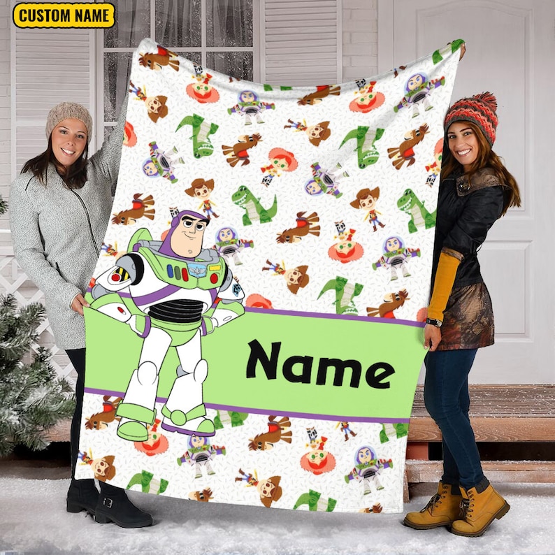 May include: A white fleece blanket featuring a repeating pattern of Toy Story characters including Buzz Lightyear, Woody, and Rex. A large Buzz Lightyear graphic stands on the left, with a lime green horizontal banner displaying the text Name.