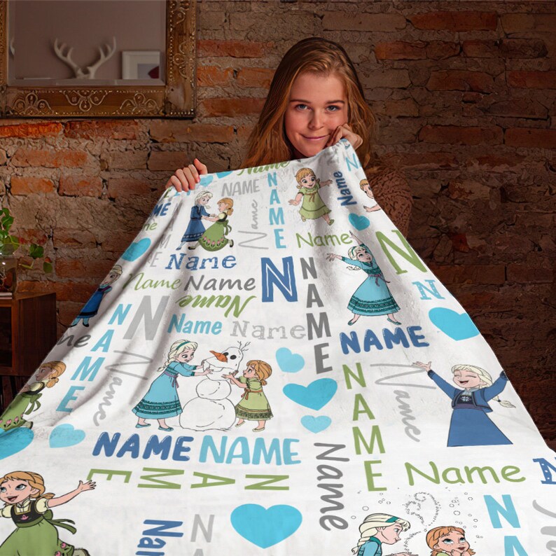May include: A white fleece blanket featuring a repeating pattern of cartoon characters in blue and green dresses, a snowman, and light blue hearts. The word Name is printed repeatedly in various blue, green, and gray fonts across the fabric surface.