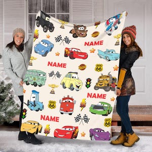 May include: A white fleece blanket with a colorful Cars theme. The blanket features various Cars characters, including Lightning McQueen, Mater, and the other racers. The blanket also has the words "NAME" and "ROUTE 66" printed on it.