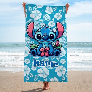 May include: A blue beach towel featuring a cartoon character with large ears, holding a flower. The towel has a turquoise background with white hibiscus flowers and the word "Name" in blue.