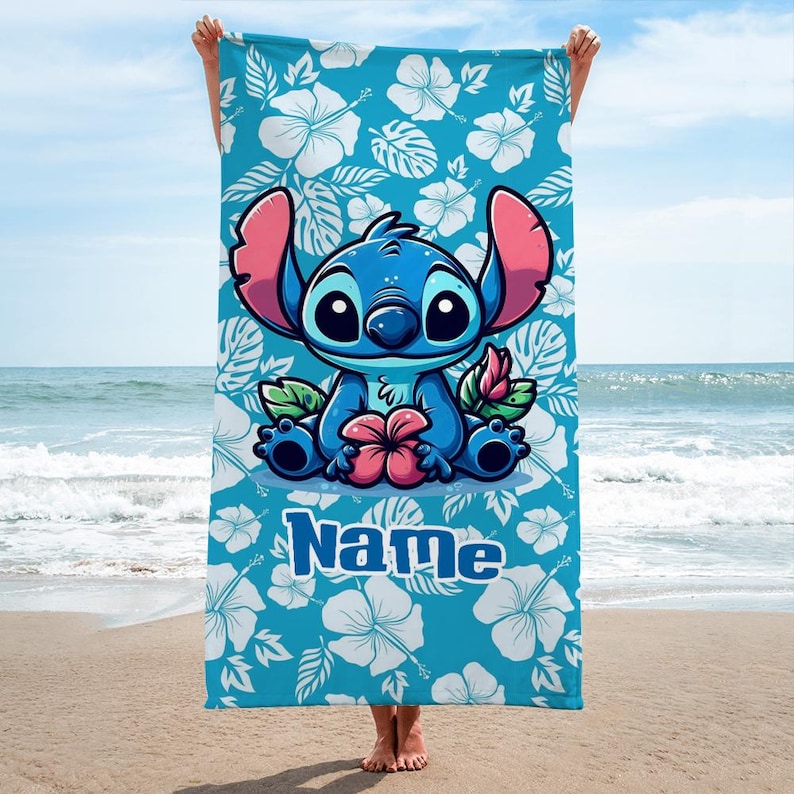 May include: A blue beach towel featuring a cartoon character with large ears, holding a flower. The towel has a turquoise background with white hibiscus flowers and the word "Name" in blue.