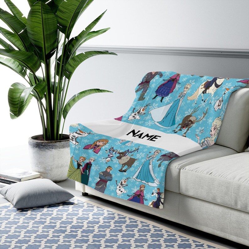Pu&ograve; includere: Una coperta azzurra con un motivo ripetuto di personaggi del film Frozen, tra cui Elsa, Anna, Olaf, Kristoff e Sven, su uno sfondo bianco con fiocchi di neve e una fascia orizzontale bianca centrale con la scritta NAME.