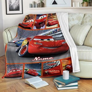 Puede incluir: Una manta de forro polar suave con un collage de Rayo McQueen de la pel&iacute;cula Cars. El dise&ntilde;o incluye varias escenas de carreras, un coche de carreras rojo grande en el centro y la palabra Name impresa en letra blanca sobre un fondo gris.