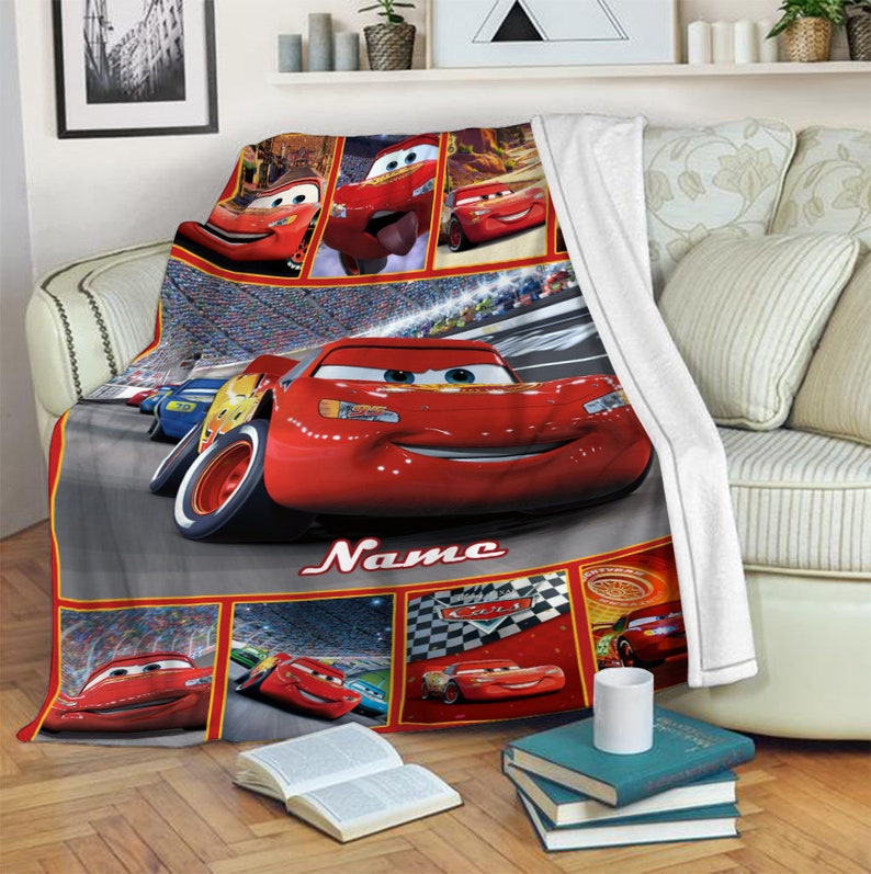Puede incluir: Una manta de forro polar suave con un collage de Rayo McQueen de la pel&iacute;cula Cars. El dise&ntilde;o incluye varias escenas de carreras, un coche de carreras rojo grande en el centro y la palabra Name impresa en letra blanca sobre un fondo gris.