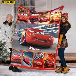 Puede incluir: Una manta de forro polar roja con varias escenas del personaje Rayo McQueen de la pel&iacute;cula Cars, incluida una gran imagen central del coche de carreras en una pista, con el texto Name y un recuadro amarillo con CUSTOM NAME.