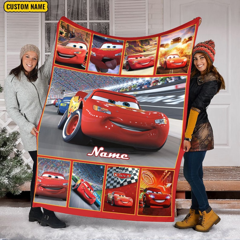 Puede incluir: Una manta de forro polar roja con varias escenas del personaje Rayo McQueen de la pel&iacute;cula Cars, incluida una gran imagen central del coche de carreras en una pista, con el texto Name y un recuadro amarillo con CUSTOM NAME.