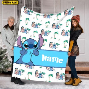 K&ouml;nnte beinhalten: Eine wei&szlig;e Fleecedecke mit einem sich wiederholenden Muster aus der blauen Figur Stitch und Palmen. Ein breites blaues horizontales Band in der Mitte zeigt das Wort Name in wei&szlig;en Buchstaben, mit einer gro&szlig;en Stitch-Grafik dar&uuml;ber.