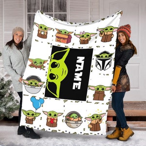 May include: A white fleece blanket featuring a repeating pattern of green alien characters in various poses, including one in a box labeled 'Adopt this baby JEDI!', one with a blue balloon, and one with a heart. A large black rectangle displays the word 'NAME'.