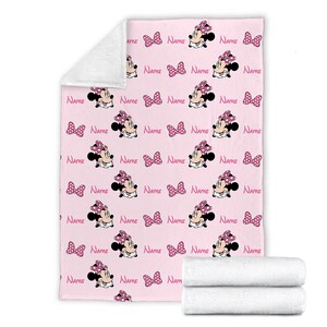 May include: Pink fleece blanket with a repeating pattern of Minnie Mouse wearing a pink bow and polka dot dress. The text "NAME" is repeated throughout the pattern.