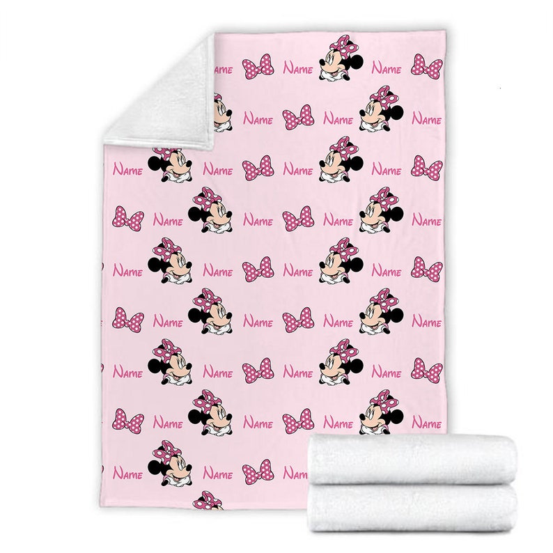 May include: Pink fleece blanket with a repeating pattern of Minnie Mouse wearing a pink bow and polka dot dress. The text "NAME" is repeated throughout the pattern.