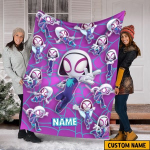 May include: A pink and purple fleece blanket with a white spider-person character design. The character is repeated multiple times on the blanket. The blanket has a blue web design and the text "NAME" is printed on the blanket.