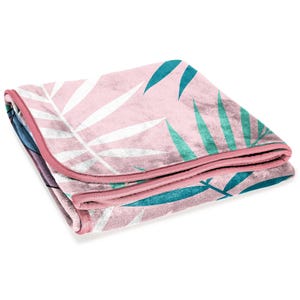 K&ouml;nnte beinhalten: Gefaltete rosa Decke mit einem botanischen Blattmuster in Wei&szlig; und T&uuml;rkis. Die Decke hat einen rosa Rand und besteht aus einem weichen Material. Das Design hat ein tropisches Thema.