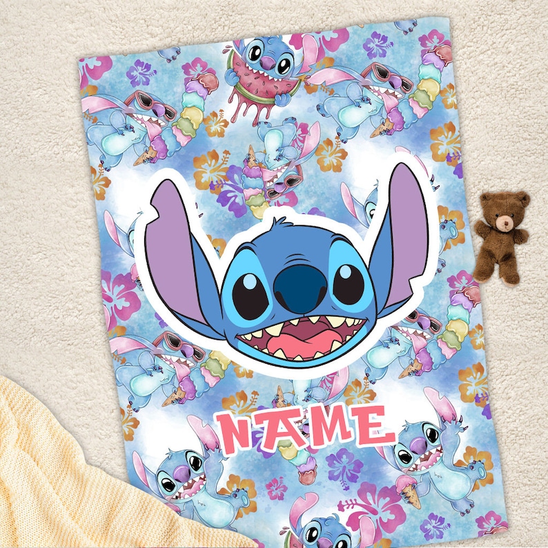 Puede incluir: Una manta rectangular con un patr&oacute;n repetitivo del personaje azul Stitch con orejas rosas, comiendo helado y sand&iacute;a, sobre un fondo azul claro con flores de hibisco naranjas y rosas y la palabra NAME en color rosa.