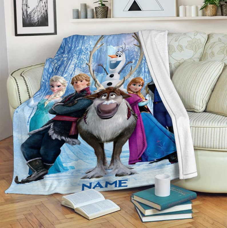 May include: A soft fleece throw blanket featuring a printed graphic of characters from Frozen, including Elsa, Anna, Kristoff, Sven, and Olaf, set against a snowy blue background with the word NAME printed in blue at the bottom center.