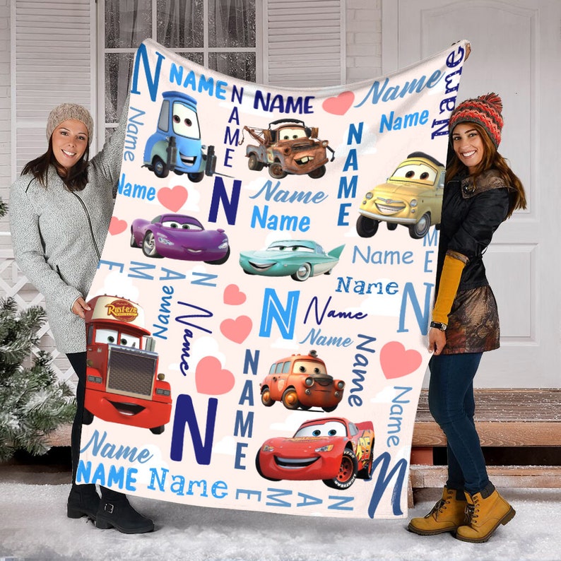 May include: A white fleece blanket featuring a repeating pattern of characters from the movie Cars, including Lightning McQueen, Mater, and others. The design incorporates the word Name in blue text, the letter N, and pink hearts throughout.