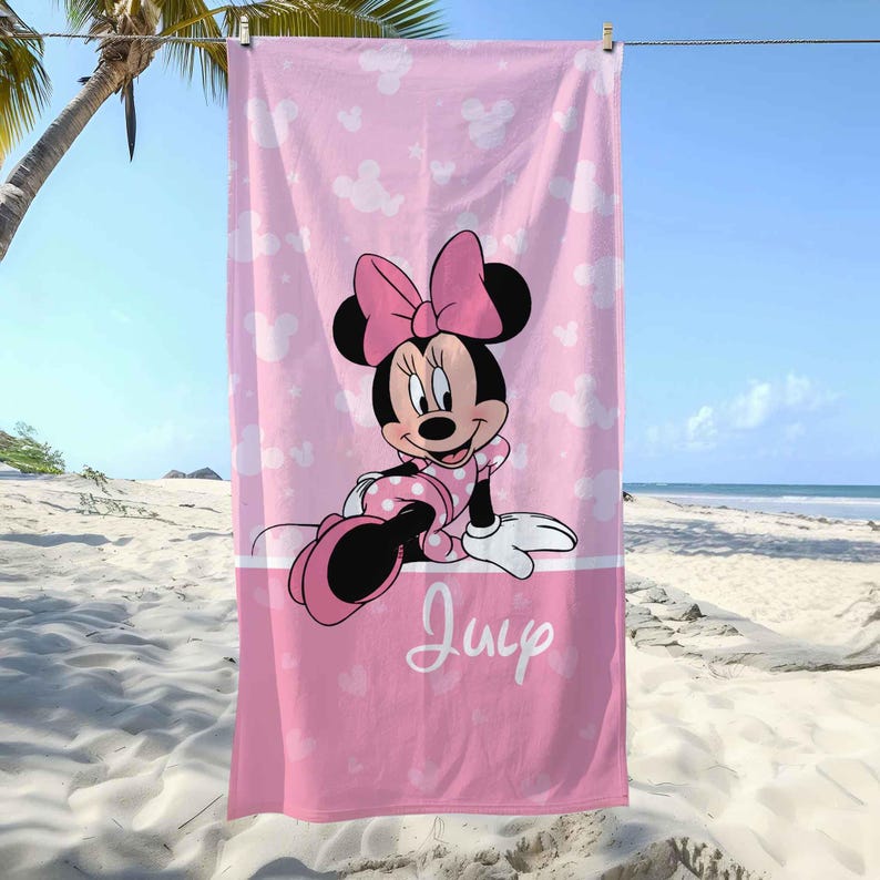 Puede incluir: Una toalla de playa rectangular en tonos rosa con un patr&oacute;n repetitivo de siluetas de Minnie Mouse y estrellas blancas. El centro muestra un gr&aacute;fico de Minnie Mouse con un vestido de lunares y un lazo rosa, con el nombre Julie en letra cursiva blanca.