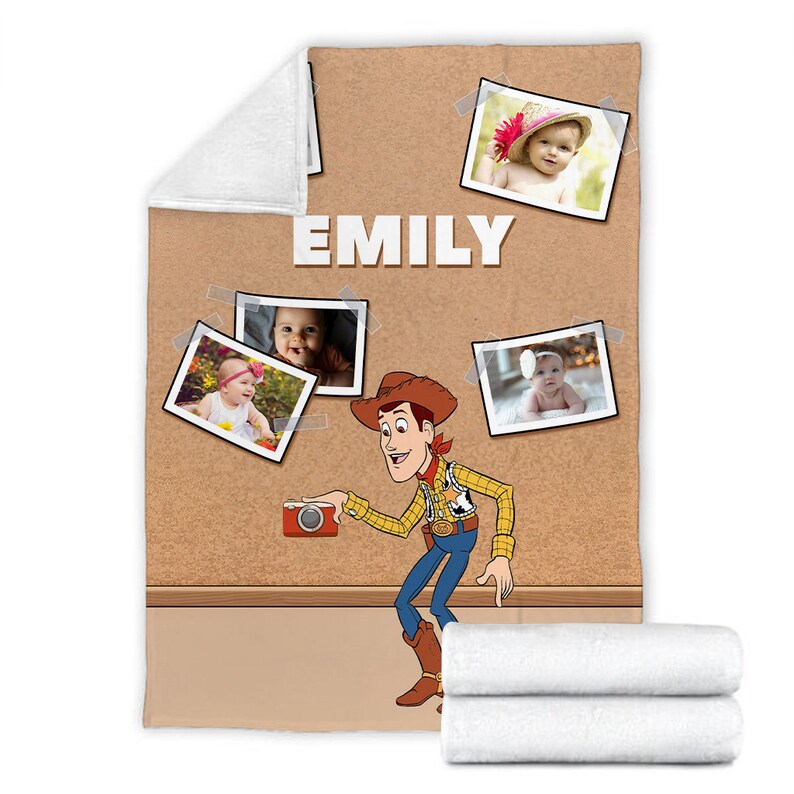 May include: A brown and tan fleece blanket with a corkboard design. The blanket features a cartoon image of Woody from Toy Story holding a camera. There are five photos of babies pinned to the corkboard. The name "EMILY" is printed in white letters on the corkboard.