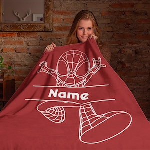 May include: A deep red fleece blanket featuring a white line art illustration of a superhero character in a webbed suit. The design includes a horizontal banner across the center with the word Name printed in bold white capital letters.