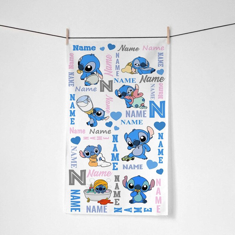 K&ouml;nnte beinhalten: Ein wei&szlig;es, rechteckiges Handtuch mit einem sich wiederholenden Muster der blauen Figur Stitch in verschiedenen Posen, unter anderem mit einer Babyflasche, beim Spielen mit einem Spielzeugauto und in einer Badewanne. Das Design enth&auml;lt blaue Herzen und das Wort Name.
