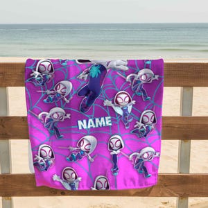 K&ouml;nnte beinhalten: Ein rechteckiges Strandtuch mit einem leuchtend pinkfarbenen Hintergrund und einem wiederkehrenden Muster aus Zeichentrickfiguren in wei&szlig;en, violetten und blauen Anz&uuml;gen, &uuml;berlagert von einem hellblauen Spinnennetz-Design und dem Wort NAME.