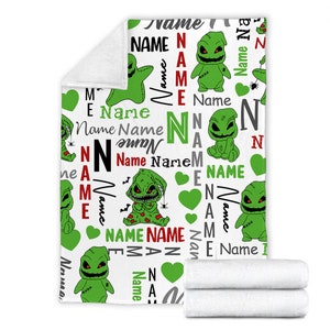 May include: White fleece blanket with a repeating pattern of green and black cartoon characters with the name "Name" repeated throughout the design.