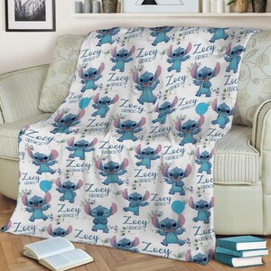 May include: A white fleece blanket featuring a repeating pattern of the blue character Stitch in various poses, interspersed with the name Zoey Grace in a blue script font and small green leaf accents, creating a playful and personalized design.