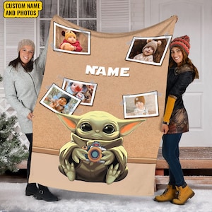 May include: A brown fleece blanket with a corkboard design featuring a cartoon image of a green alien holding a camera. The corkboard has several photos of babies pinned to it. The text "NAME" is printed on the corkboard.