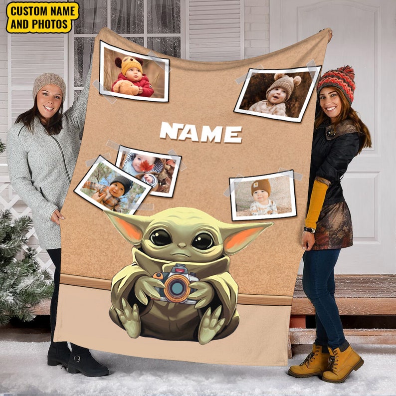 May include: A brown fleece blanket with a corkboard design featuring a cartoon image of a green alien holding a camera. The corkboard has several photos of babies pinned to it. The text "NAME" is printed on the corkboard.