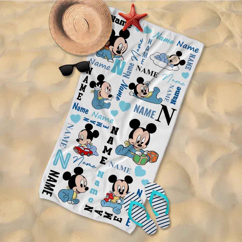 May include: A white beach towel with a blue and white pattern featuring Mickey Mouse characters. The towel has the word "Name" repeated throughout the design.