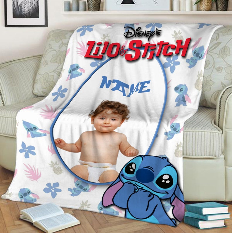 K&ouml;nnte beinhalten: Eine wei&szlig;e Fleecedecke mit einem wiederkehrenden Muster aus blauen Stitch-Figuren, rosa Palmbl&auml;ttern und blauen Blumen. Die Decke zeigt das Disney's Lilo & Stitch-Logo, einen zentralen ovalen Rahmen mit dem Wort NAME und ein Babyfoto.