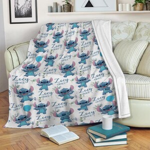 May include: A white fleece blanket featuring a repeating pattern of the blue character Stitch from Lilo & Stitch, interspersed with blue balloons, green leaves, and the personalized text Zoey Grace in a dark blue cursive script font.