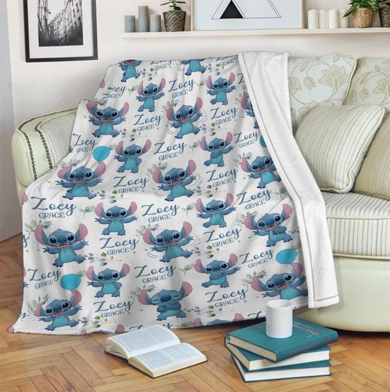 May include: A white fleece blanket featuring a repeating pattern of the blue character Stitch from Lilo & Stitch, interspersed with blue balloons, green leaves, and the personalized text Zoey Grace in a dark blue cursive script font.