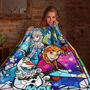 Pode incluir: Uma manta macia com um gr&aacute;fico vibrante em estilo de vitral de Elsa, Anna e Olaf de Frozen. O design inclui padr&otilde;es geom&eacute;tricos coloridos, flocos de neve e a palavra NAME na parte inferior em letras mai&uacute;sculas azul-claras.