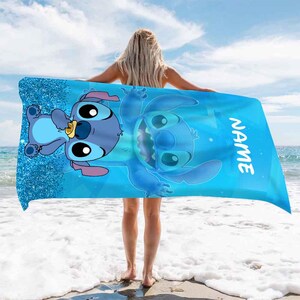 Puede incluir: Una toalla de playa azul con un fondo de brillo que presenta un personaje de dibujos animados de Stitch. La toalla tiene la palabra "NAME" impresa en el lado derecho.
