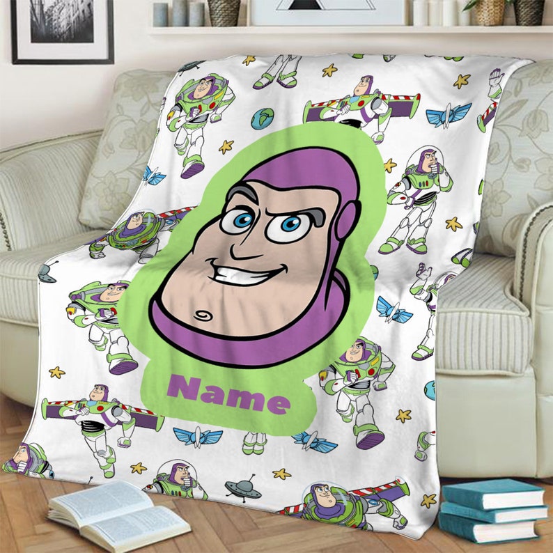 May include: A white fleece blanket featuring a repeating pattern of Buzz Lightyear in various poses, small yellow stars, and blue wings. A large central lime green shape displays a cartoon portrait of Buzz Lightyear and the word Name.
