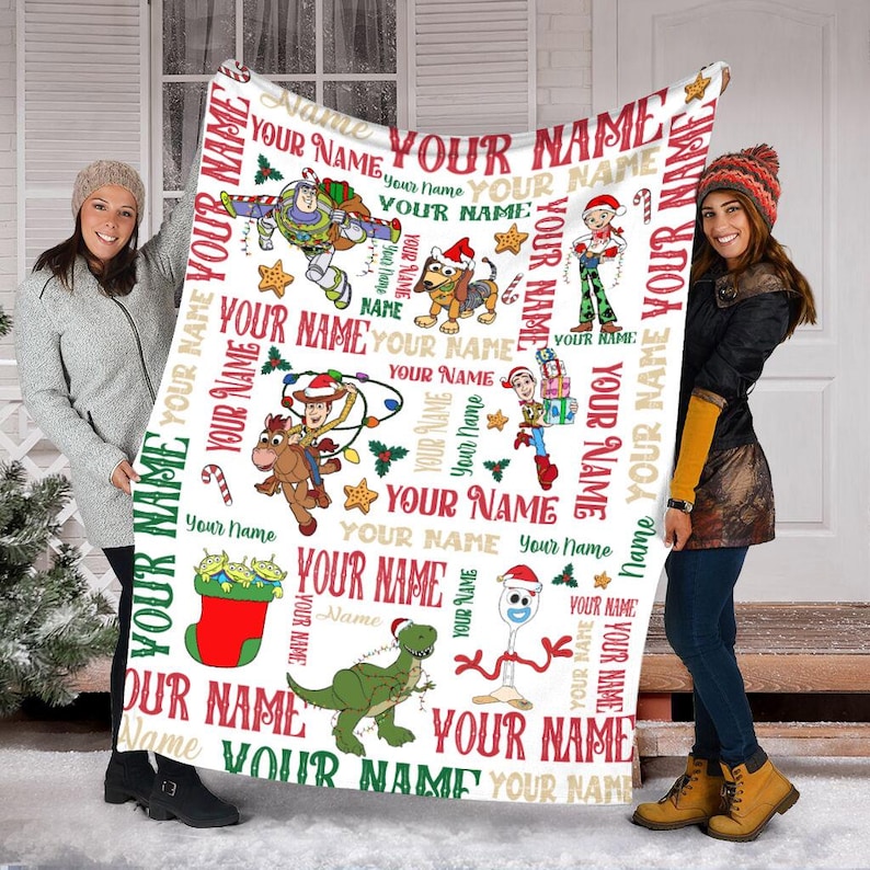 May include: White fleece blanket with a Christmas themed pattern featuring characters from the Toy Story franchise. The blanket is decorated with red, green, and gold accents. The text "YOUR NAME" is repeated throughout the blanket.