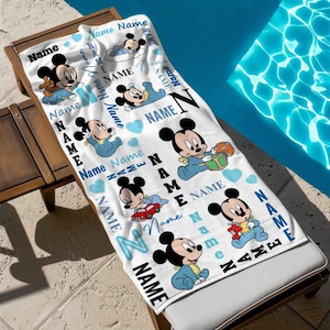 May include: White beach towel with a blue and white pattern featuring Mickey Mouse characters. The towel has the word "Name" repeated throughout the design.