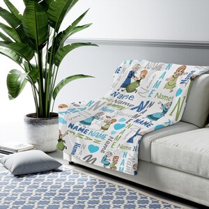 May include: A white throw blanket featuring a repeating pattern of two cartoon characters in blue and green dresses, a snowman, blue hearts, and the word Name in various blue, green, and grey fonts, arranged in a scattered, multi-directional layout.