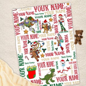 May include: A white fleece blanket with a Christmas themed pattern featuring Toy Story characters. The blanket is covered in the words "Your Name" in red, green, and gold.