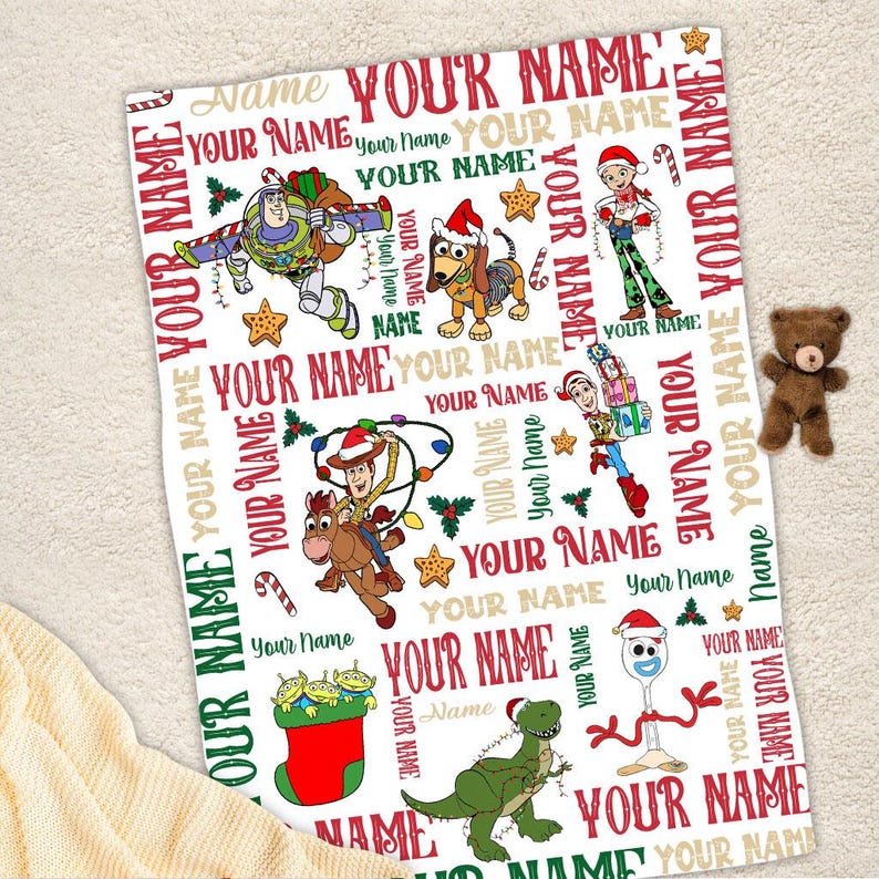 May include: A white fleece blanket with a Christmas themed pattern featuring Toy Story characters. The blanket is covered in the words "Your Name" in red, green, and gold.
