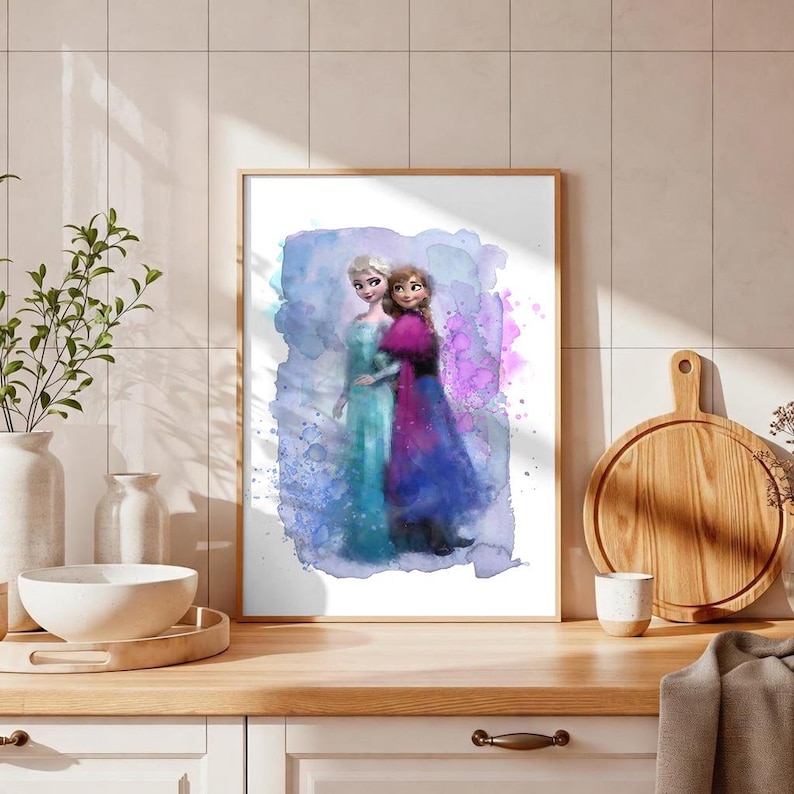 May include: Watercolor print of two women in long dresses, framed in a gold-colored frame. The women are depicted in shades of blue, purple, and pink, set against a blue and purple watercolor background. The artwork is displayed on a wooden surface.