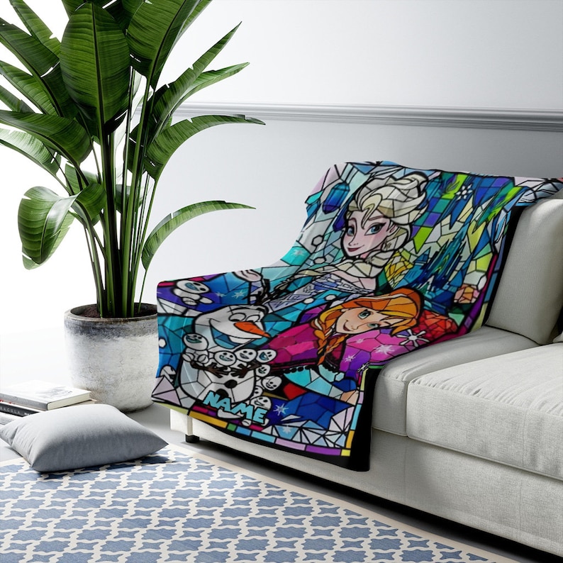 Pode incluir: Uma manta macia com um gr&aacute;fico colorido em estilo vitral que mostra Elsa, Anna e Olaf de Frozen. O design geom&eacute;trico em tons de azul, roxo e rosa inclui a palavra NAME impressa em azul claro na parte inferior da pe&ccedil;a.