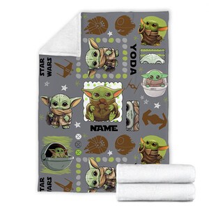 May include: A gray fleece blanket featuring a repeating pattern of green alien characters, Star Wars icons, and the text "STAR WARS", "YODA", and "NAME". The design includes various illustrations of the character in robes and pods on a gray background.