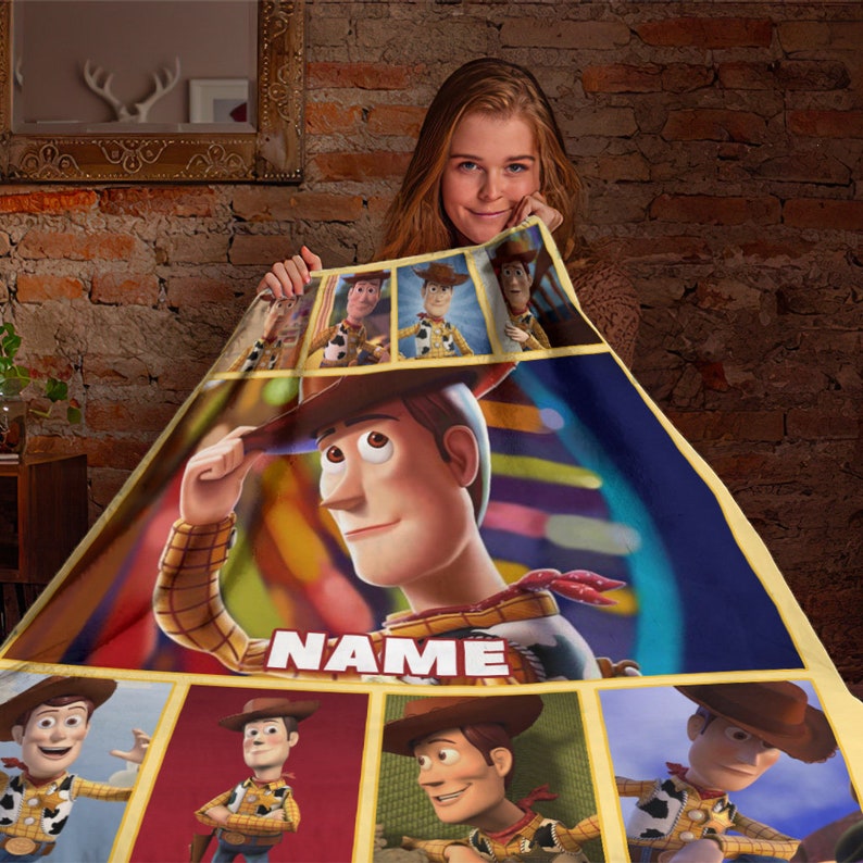 May include: A soft fleece blanket featuring multiple panels of the character Woody from Toy Story. The design includes a large central image of Woody with a white text box labeled NAME, surrounded by smaller rectangular frames of the character.