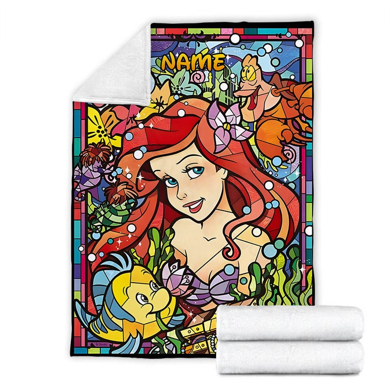 Puede incluir: Una manta rectangular de forro polar con una vibrante ilustraci&oacute;n estilo vidriera de una sirena pelirroja, un pez amarillo y azul y un cangrejo. La palabra NAME est&aacute; impresa en amarillo en la parte superior. La manta tiene un reverso de felpa blanco.